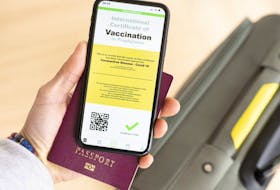 Overhead view of a person holding a passport and a smart phone with a digital illustration of an example of a certificate of vaccination against COVID-19.
