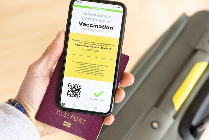 Overhead view of a person holding a passport and a smart phone with a digital illustration of an example of a certificate of vaccination against COVID-19.