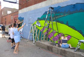 Jaimie Peerless of Phantom Studio talks to one of her helpers as the mural in homage to Theresa McAuley Robinson takes shape behind Main Street Station in Kentville.