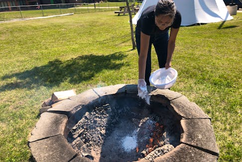 Kelly Sark covers bannock with flour as she places it in the fire to cook at the Lennox Island FIrst Nation's guided experience called Bannock and Clams on the Sand at the Mi’kmaq Culture Centre. Indigenous tourism - once a fast-growing sector - has been hard hit by the pandemic. - Helen Earley