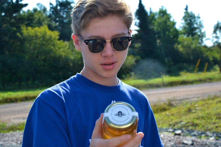 Devon Touesnard, a summer student at the Potlotek greenhouse, checks out a bottle of honey from the beehives nearby. Touesnard said he got an early taste when he tried some of the honey straight from a piece of the comb a couple of weeks ago. ARDELLE REYNOLDS/CAPE BRETON POST