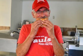 Longtime Paul’s Food Factory employee Paul Gardiner sinks his teeth into the Whitney Pier business’ signature product – the pizza burger. CBRM council recently voted to make the popular snack the official food of the municipality for 2021. DAVID JALA/CAPE BRETON POST