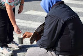 A woman puts a coin in a panhandler's cup.