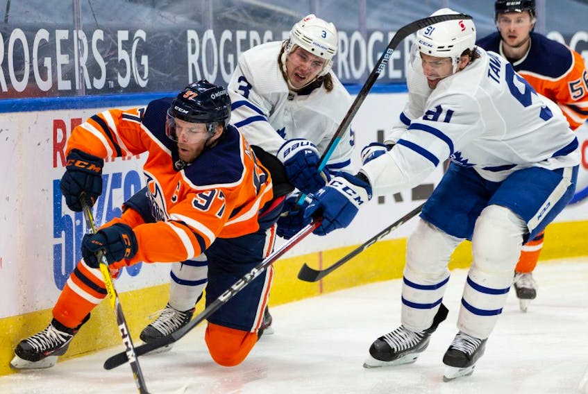 Edmonton Oilers’ Connor McDavid (97) battles Toronto Maple Leafs’ Justin Holl (3) and John Tavares (91) during third period NHL action at Rogers Place in Edmonton, on Monday, March 1, 2021. 