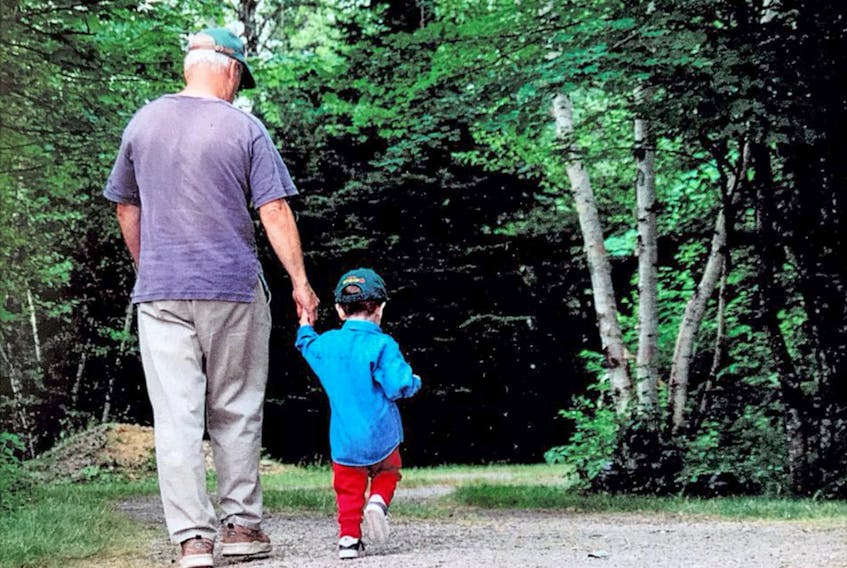 Ray McNabb, left, holds the hand of his grandson, then-two-year-old Graeme McNabb, as the pair walk down the front lane at Ray's cottage to pick up the Cape Breton Post from the driveway, in Sangaree in July, 2001. CONTRIBUTED