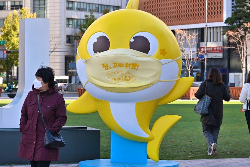 People walk past a shark character from the children's song "Baby Shark" at Seoul Plaza in Seoul on November 3, 2020.