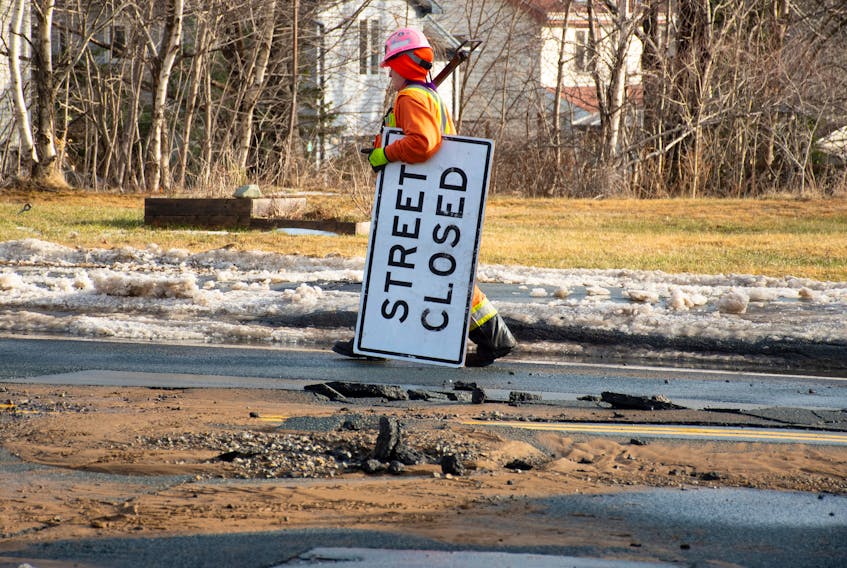 A worker carries a street closed sign as Halifax Water crews get ready to repair a water main break on Herring Cove Rd. near Osborne St. on Tuesday, Jan. 18, 2022. Water service in the Cowie Hill area has been temporarily shut down.