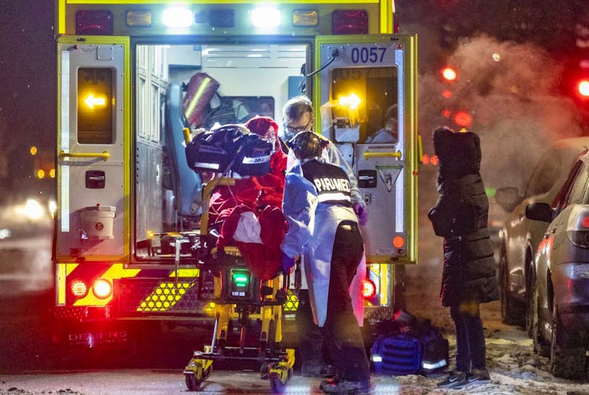 A woman watches paramedics load a COVID patient into an ambulance in Montreal Wednesday Jan. 12, 2022.