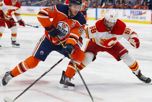 Edmonton Oilers forward Connor McDavid (97) tries to carry the puck around Calgary Flames defencemen Oliver Kylington at Rogers Place in Edmonton on Saturday, Jan. 22, 2022.