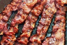 Bacon slices are cooked in a pan.