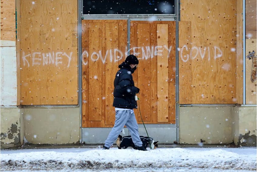  A person walks their dog past graffiti on a boarded up building near 103 Avenue and 106 Street, in Edmonton on Wednesday, Jan. 26, 2022.