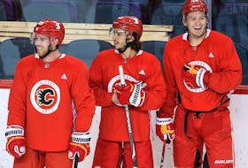 The Calgary Flames’ Elias Lindholm, Johnny Gaudreau and Matthew Tkachuk smile during a break in practice during training camp in Calgary on Jan. 4, 2021. 
