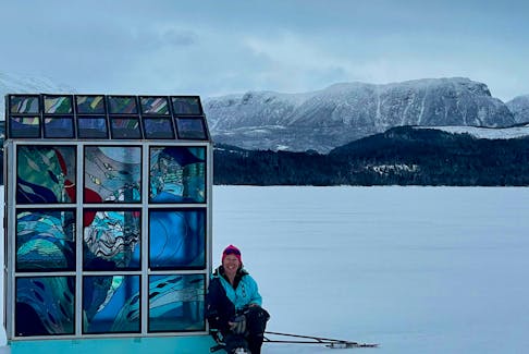 Rocky Harbour artist Urve Manuel sits next to her latest creation, a full-size stained-glass ice-fishing shack, that she installed on Rocky Harbour Pond recently. Her plan is to assemble it in various locations around the community throughout the winter. 