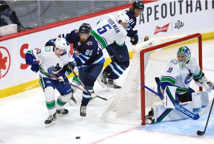Winnipeg Jets centre Pierre-Luc Dubois (second from left) lays the lumber on Vancouver Canucks defenceman Quinn Hughes (left) in Winnipeg on Jan. 27.