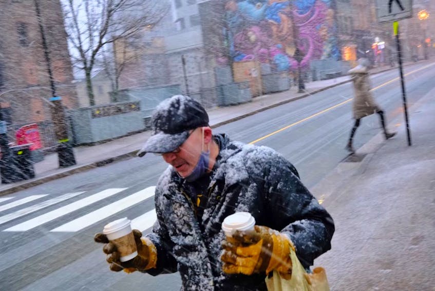 A man carries two coffees through the start of a snowstorm in downtown Halifax on Friday, Jan. 7, 2021.