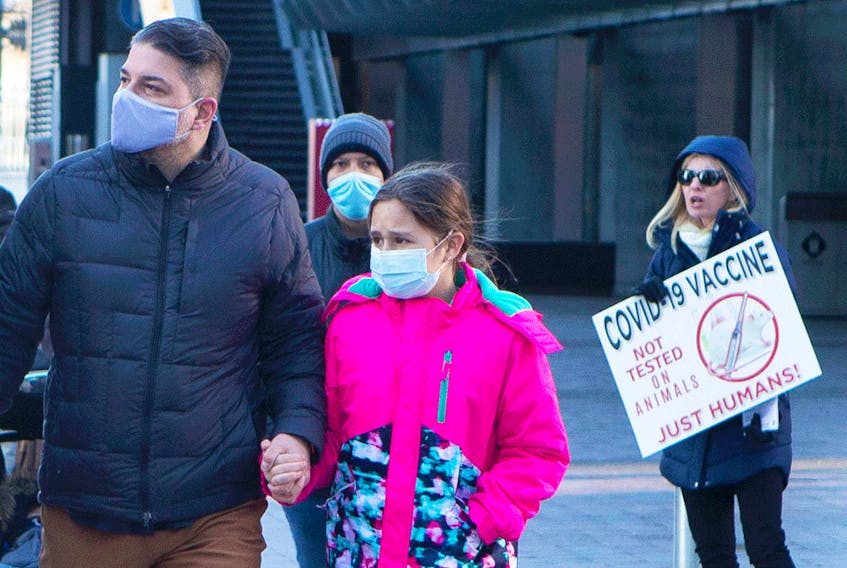 People walk past an anti-vaccine protester as they walk towards a children's COVID-19 vaccine clinic in Toronto.