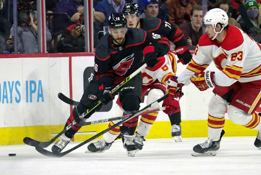 Carolina Hurricanes centre Vincent Trocheck, left, and right wing Jesper Fast, back center, battle Calgary Flames centre Sean Monahan for the puck at PNC Arena in Raleigh, N.C., on Friday, Jan. 7, 2022.