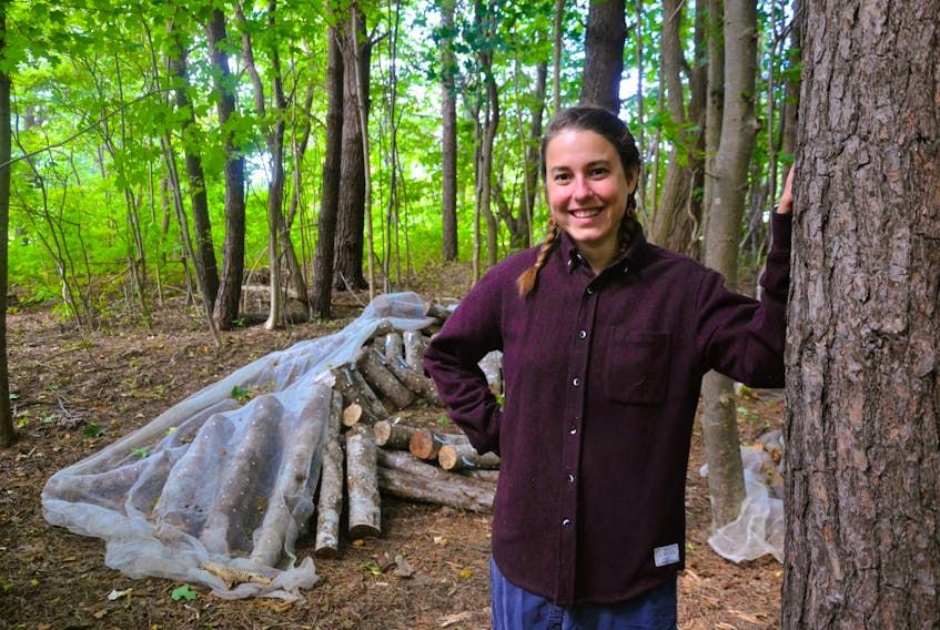 Megan Giffen, the owner of Unseen World stands in front of a pile of logs inoculated with mushrooms. -Larry Powell