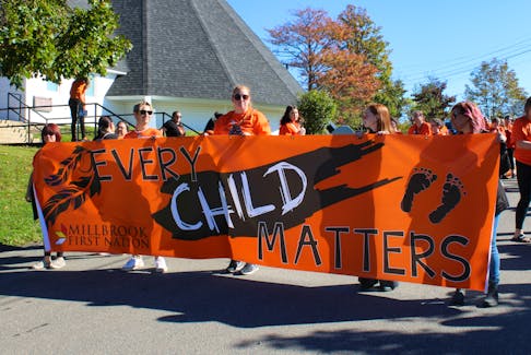 Several volunteers hold up a flag that reads "ever child matters" at the Truth and Reconciliation Day march in Millbrook.