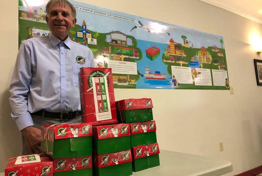 Pastor Bob Ring, Father’s Church, stacks a few Operation Christmas Child gift boxes destined for needy children while a poster in the background shows the route the boxes will take to get their destinations.