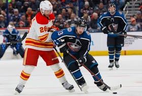 Columbus Blue Jackets forward Johnny Gaudreau, right, carries the puck across the blue line past Calgary Flames forward Elias Lindholm at Nationwide Arena in Columbus, Ohio, on Friday, Dec. 9, 2022.