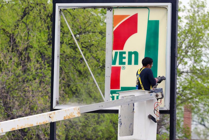 A man takes down a 7-Eleven sign in front of a now closed store in Winnipeg, in 2021.