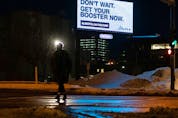  A pedestrian crosses 104 Avenue at MacEwan University while a government advertisement calling for COVID-19 booster shots to combat the Omicron strain outbreak is shines in the background in Edmonton, on Wednesday, Jan. 12, 2022. Photo by Ian Kucerak