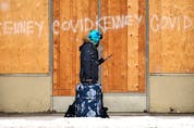 A person carries luggage past Jason Kenney and COVID-19 graffiti on a long boarded up building near 103 Avenue and 106 Street, in Edmonton on Wednesday, Jan. 26, 2022. Photo by David Bloom