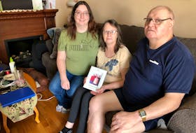 Michael Tutty's family say they can't begin to heal from the 41-year-old's tragic death until the driver of the vehicle that hit him if found. Pictured here in the living room of their Glace Bay home on Feb. 17, from left, Michael's sister Stephanie Tutty, his mother Angela Tutty and his father Melvin Tutty. Angela is holding a photo of the four of them from 2012. NICOLE SULLIVAN/CAPE BRETON POST