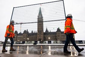  Workers carry a piece of fencing to shore up existing barricades on Parliament Hill, Feb. 17, 2022.