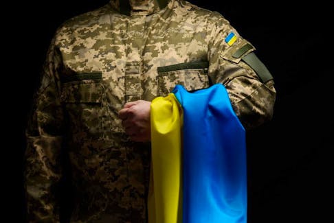 a soldier of the Ukrainian armed forces stands with a blue-yellow flag of Ukraine on a black background. Honoring veterans and commemorating those killed in the war