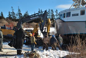 People watch as two excavators finish getting the Lady Annette II ashore at the Lower East Pubnico  wharf on Jan. 31. The vessel sank at the wharf on Jan. 30 after parting its lines as the area experienced a severe winter storm over that weekend. KATHY JOHNSON