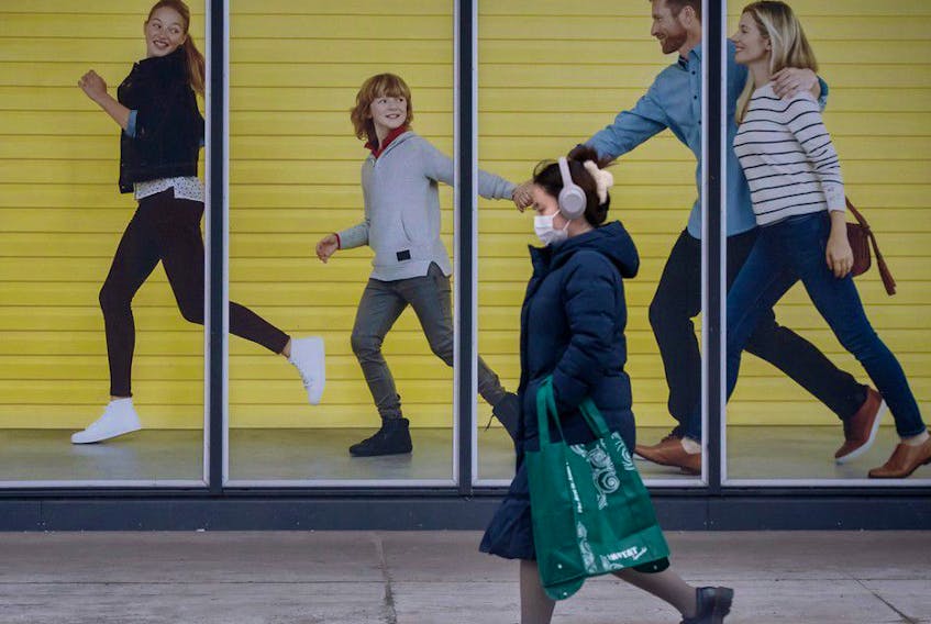 A pedestrian wearing a mask walks past a mural of a family enjoying a leisurely massless walk in Toronto during the COVID-19 pandemic, Thursday February 3, 2022.
