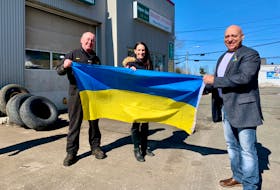 Broadway Auto Repair shop owner Blaine Campbell, left, says he’s only too happy to display the Ukrainian flag at his Whitney Pier service station. Campbell, who was raised in the neighbourhood, says he has always known area residents of Ukrainian descent and that many remain a regular customers. The flag was delivered by CBRM District 12 councillor Lorne Green, above right, and Michelle Wilson, centre, executive director of the Sydney Downtown Development Association. Both are also residents of Whitney Pier, the Sydney neighbourhood where the majority of Ukrainians, among the many ethnicities that also came, settled when they began arriving more than a century ago to work at the nearby steel mill. Flags were delivered to businesses along Victoria Road and on Charlotte Street in downtown Sydney. DAVID JALA/CAPE BRETON POST  