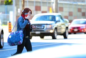 A woman wearing headphones crosses the street at a Toronto intersection. Studies show drivers of larger pickups and SUVs have a harder time seeing pedestrians, particularly when making turns. Craig Robertson/Postmedia News