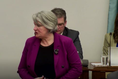 Finance Minister Darlene Compton, foreground, speaks in the P.E.I. legislature in this screenshot. Justice Minister Bloyce Thompson, back left, and Education Minister Natalie Jameson are visible behind her without their masks on but MLA Sidney MacEwen, right, is wearing his. 