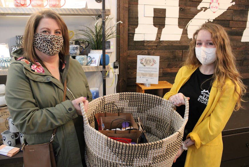 The Lotus Centre executive director Michaela MacLachlan and Megan Johnson of My Home Mercantile hold up a basket collecting hygiene care kits. 