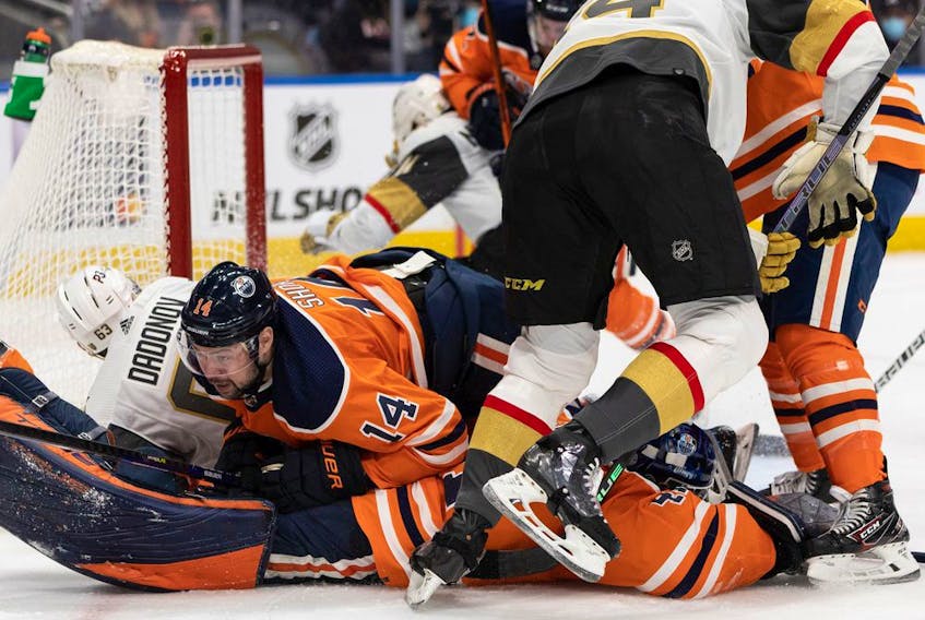 Edmonton Oilers' Devin Shore (14) lands on goaltender Mike Smith (41) as they play the Las Vegas Golden Knights at Rogers Place in Edmonton on Feb. 8, 2022.