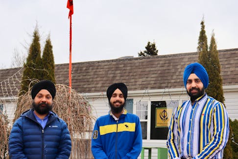 Prabhjot Singh, right, says gurudwaras across the world fly an orange flag (visibile in the background) called nishan sahib, which notifies people of a gurudwara in the neighborhood where they can eat and find shelter. Arshgod Singh stands in the middle with Savneet Singh on his left, outside the Gurudwara Sahib in Stratford.