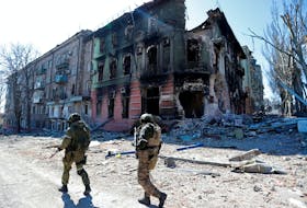Soldiers walk past a burned out building in the southeastern Ukraine city of Mariupol, April 11, 2022.