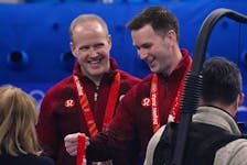 Canada’s Brad Gushue, right, looks at a bronze medal with teammate Mark Nichols by his side, at the Beijing Winter Olympics on Feb. 19, 2022.
