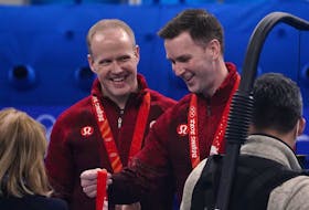 Canada’s Brad Gushue, right, looks at a bronze medal with teammate Mark Nichols by his side, at the Beijing Winter Olympics on Feb. 19, 2022.