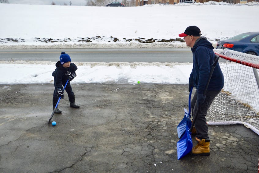 Jase Steele, left,  prepares to fire a close-range shot at the net guarded by his shovel-wielding grandfather, John Boutilier, on Tuesday in Sydney. The pair cleared the Alexandra Street driveway so they could play but left the snow covering the street end so stray balls wouldn’t roll onto the busy road. Steele, an eight-year-old student at nearby Shipyard Elementary, took advantage of the “snow day” to work on his shot with his grandfather. Depending on the location, the Cape Breton Regional Municipality received snowfall amounts from 12 to 19 cm. However, the heavy, wet snow was already melting by early afternoon as above freezing temperatures followed the spring snowstorm. DAVID JALA/CAPE BRETON POST