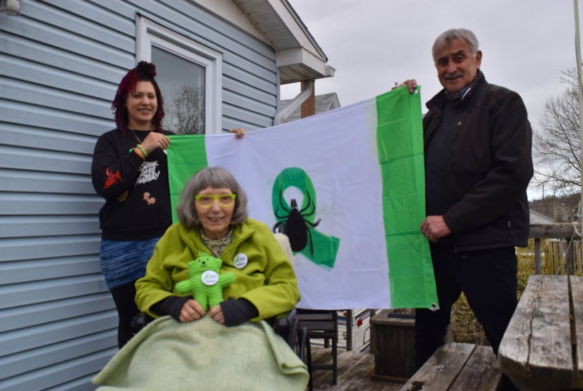 Janelle Clyke, left, and John Ashton hold a flag that was the brainchild of Brenda Sterling-Goodwin, front. Ashton, who is a graphic designer put the design onto paper and then Clyke made the flag. A duplicate is hanging at Halifax City Hall for Lyme Awarness Month.