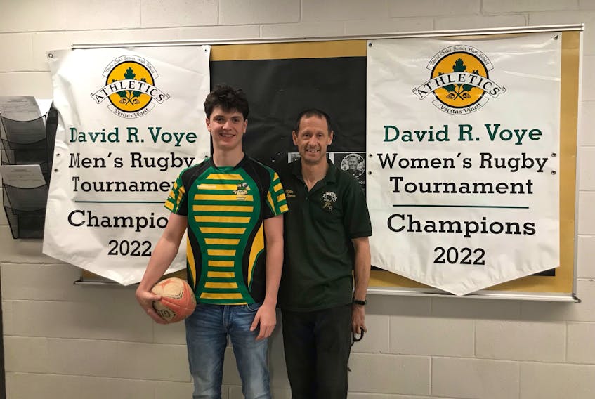 Ryan MacKinnon, left, and his father, Mike MacKinnon, pose with the championship banners for the 2022 David Voye Memorial rugby tournament at Three Oaks Senior High School in Summerside this week. Ryan is a senior with the host Three Oaks AAA Axemen, and Mike played on the first-ever boys’ senior AA rugby team at the Summerside school in 1990.