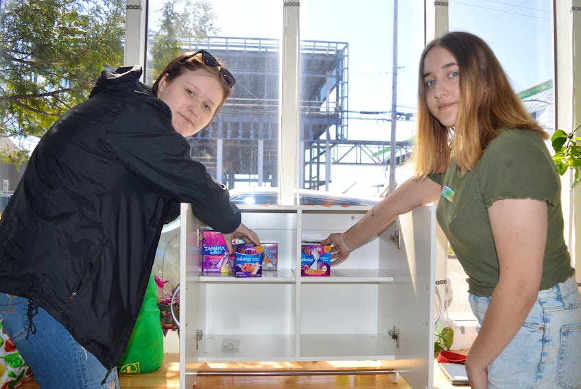 Abby MacDonald, left, and Azara Johnson, volunteers at the Cape Breton Youth Project, stock the new menstruation station at the downtown Sydney centre on Tuesday. Participants painted the cupboard that will be filled with tampons, pads, panty liners and other products to help address period poverty. Beth Steele, a participant in the Northside Changemakers program, also installed a menstruation station cupboard at Community Cares Youth Outreach in Sydney Mines. Chris Connors/Cape Breton Post