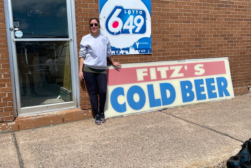 Angie Fitzpatrick stands with the iconic sign of the beer store her father, John Otis Fitzpatrick, owned on Topsail Road in St. John's until he died May 26, 2021. The sign is being auctioned, with the proceeds going to the Dr. H. Bliss Murphy Cancer Care Foundation.