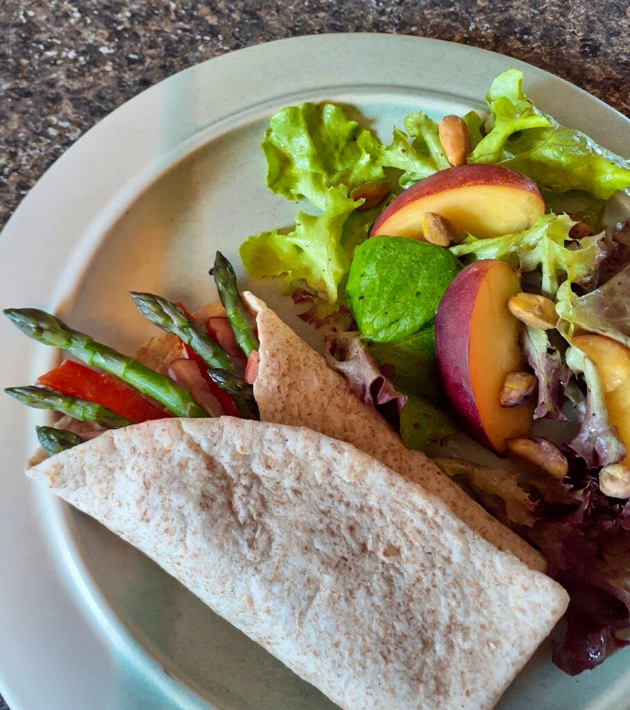 This whole wheat wrap with fresh asparagus, herbed Boursin cheese, red pepper strips and slivers of ham is served with salad of mixed greens, nectarine and pistachios.