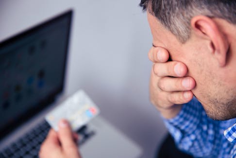 Upset man holding credit card with laptop on background  As the cost of living explodes, more and more people are looking for ways to reduce their debt quickly. - Storyblocks