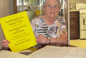 Vie Lynds, the president of the Good Neighbours club, displays a poster for an upcoming fundraiser.